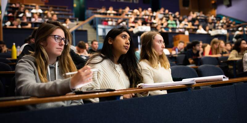 Group shot from full lecture, Three closest students are focused on with them looking onwards at the presentation